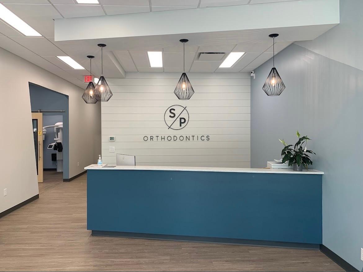 Modern orthodontic reception area of SP Orthodontics featuring a blue and white color scheme, illuminated pendant lights, and a welcoming front desk.