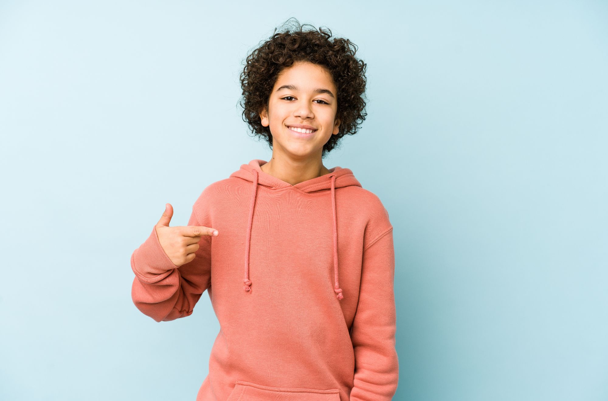 Smiling young boy in a pink hoodie, pointing at himself, representing the confidence and positive outcomes of braces treatment offered by SP Orthodontics near Indian Trail, NC.